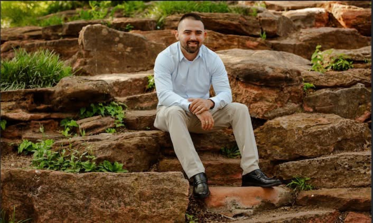 Dalton Triplett, founder of Skullco Construction, seated on sandstone steps in a light blue shirt